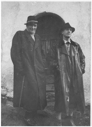 Zwei Männer mit Mänteln und Hüten vor einer alten Türe, Schwarz-Weiß-Foto