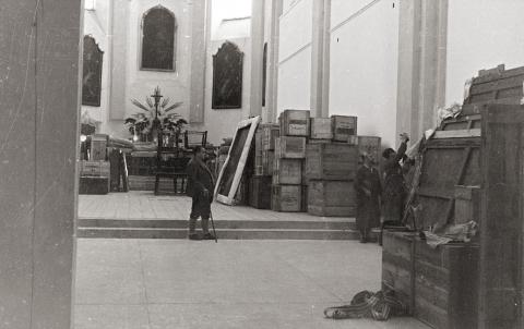 Blick in das Innere der Kirche, mit drei arbeitenden Männern, deponierten Kisten und Bildern, Schwarz-Weiß-Foto