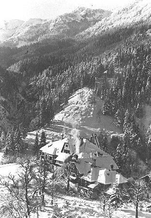 Blick in ein verschneites Tal, im Vordergrund Gebäude, Schwarz-Weiß-Foto