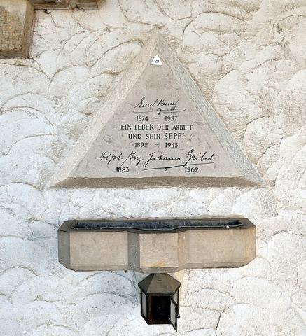In eine Wand eingelassener dreieckiger Gedenkstein mit Inschrift, darunter ein Becken und eine Laterne