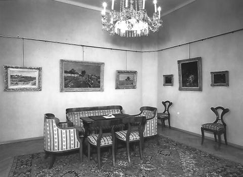 Blick in einen Raum mit Kronleuchter, Gemälden und Sitzmöbeln, Schwarz-Weiß-Foto